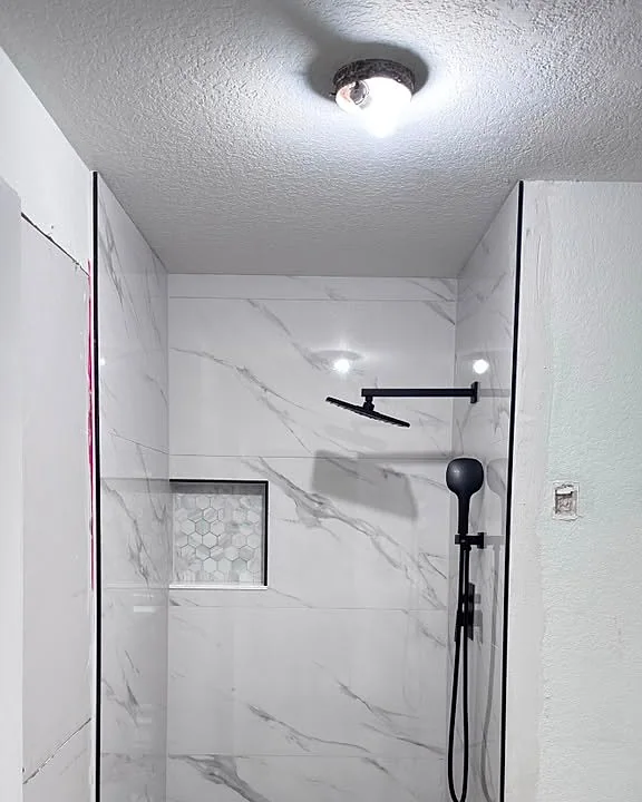 Walk-in shower finished in white marble-look tile with black fixtures and a mosaic floor