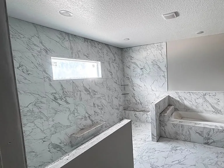 Bathroom clad in marble-look tile with a tiled bench and narrow window