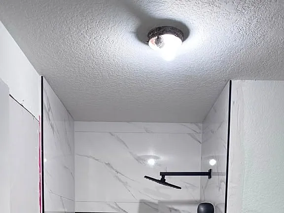 Walk-in shower with white marble-look walls, black fixtures and a mosaic floor