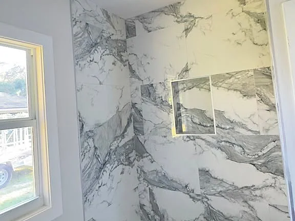Bathtub surround built from bookmatched marble-look panels beside a window