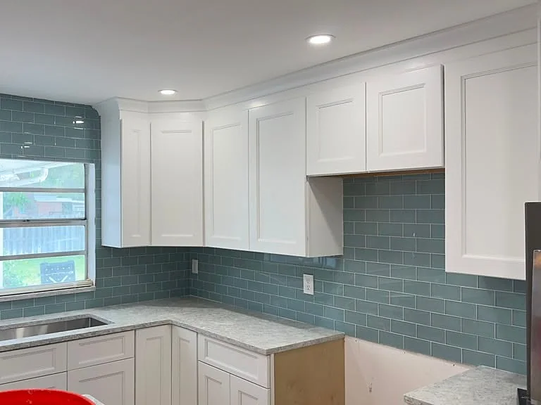 Kitchen with white shaker cabinets and a teal glass subway tile backsplash