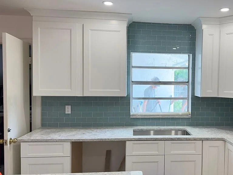Kitchen corner with white cabinets, teal tile backsplash and a window over the sink