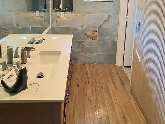 Bathroom with a long double vanity, wood flooring and marble-look shower walls