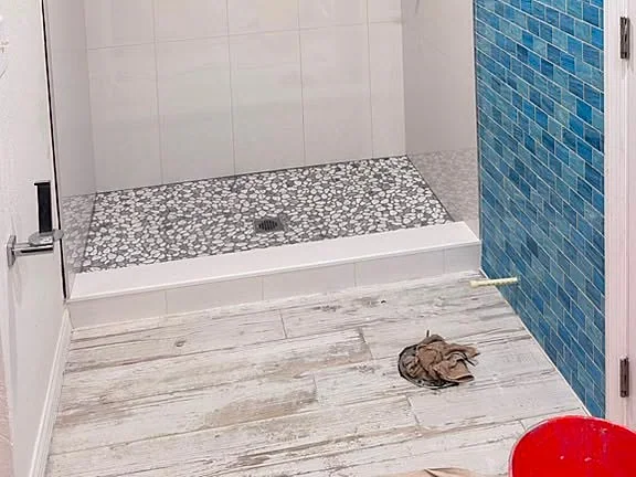 White tiled shower with a blue glass mosaic accent band and pebble floor