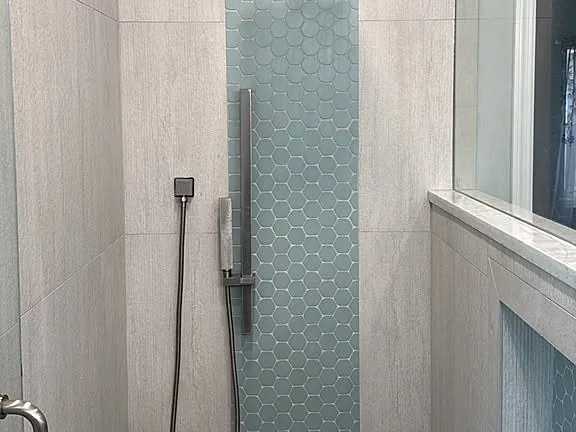 Shower with a vertical glass mosaic stripe, recessed niche and hand shower