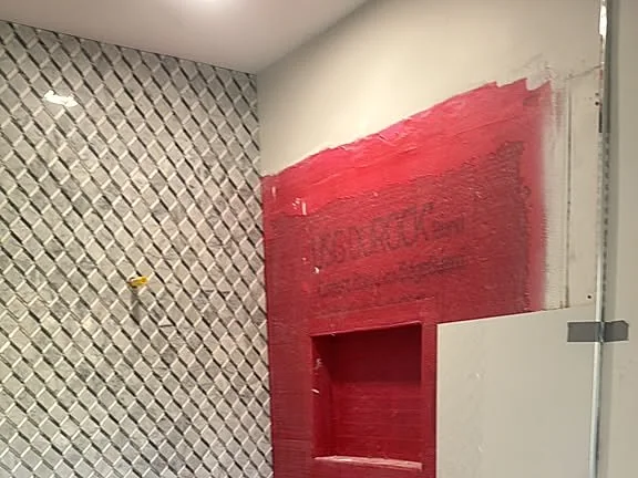 Shower mid-installation showing red waterproofing membrane behind the tile