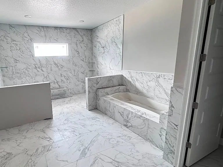 Remodeled bathroom in marble-look large-format tile with a built-in tub deck and matching floor
